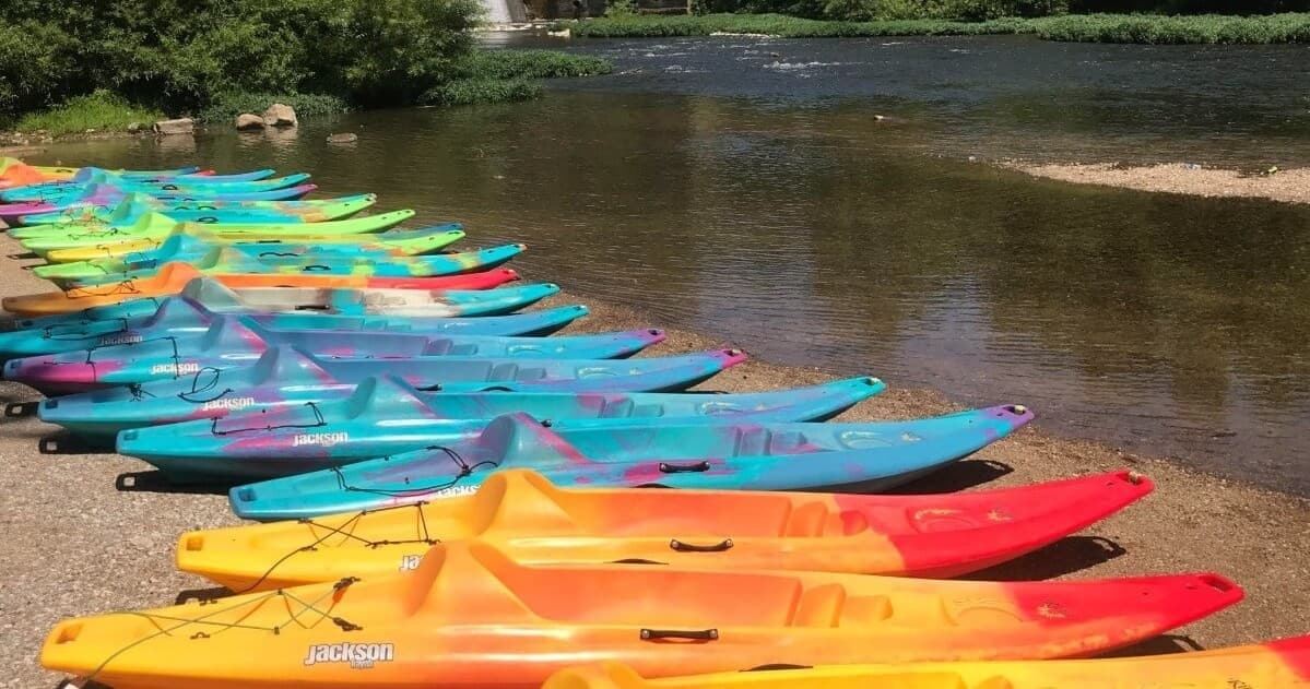 Row of colorful kayaks lined on sandy riverbank ready to rent