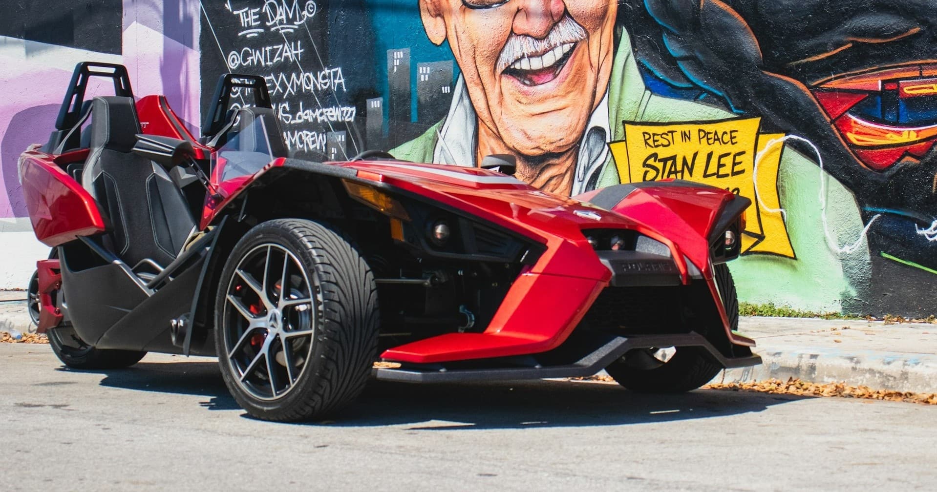 Red Slingshot parked by colorful urban mural in city streets