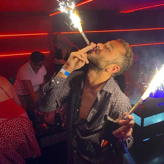 Man celebrating with sparklers and cigar in crowded nightclub scene