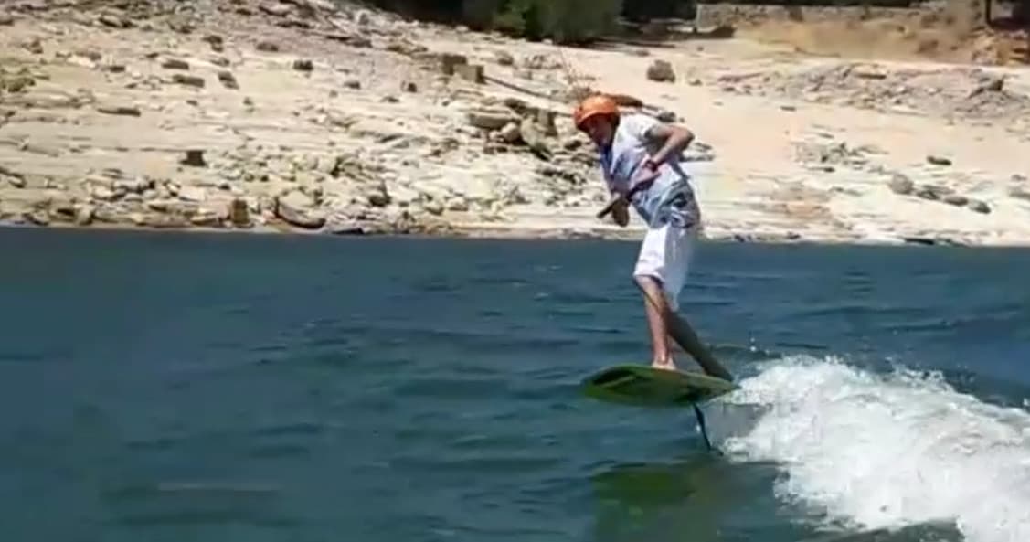 E-foil rider carving through calm reservoir waters near rocky shore