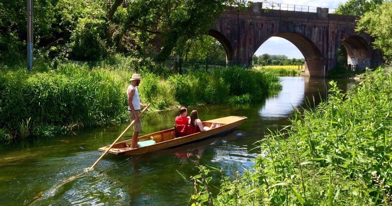 Punter steering wooden punt under brick railway bridge on river
