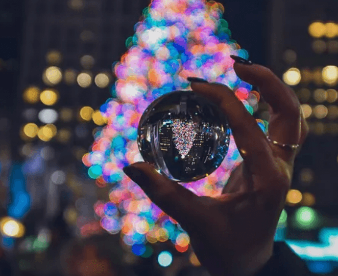 Hand holding lensball reflecting festive Christmas tree lights at night