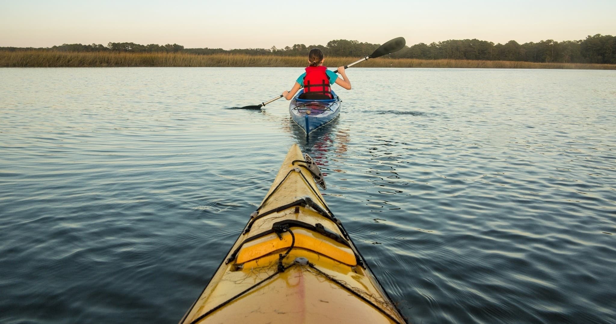 Kayaker paddling across calm bay at sunset, leading bow