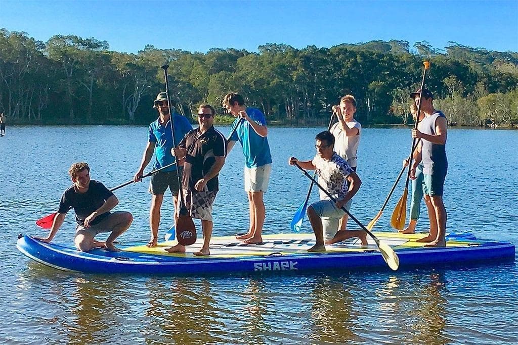 Group paddleboarding on calm lake with scenic treeline backdrop