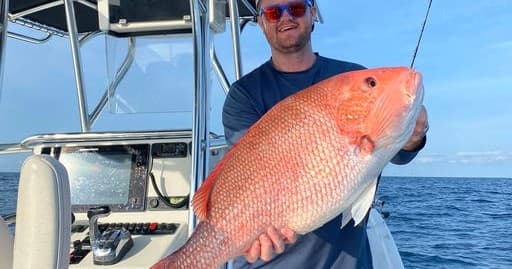 Angler holding large red snapper on offshore fishing charter boat