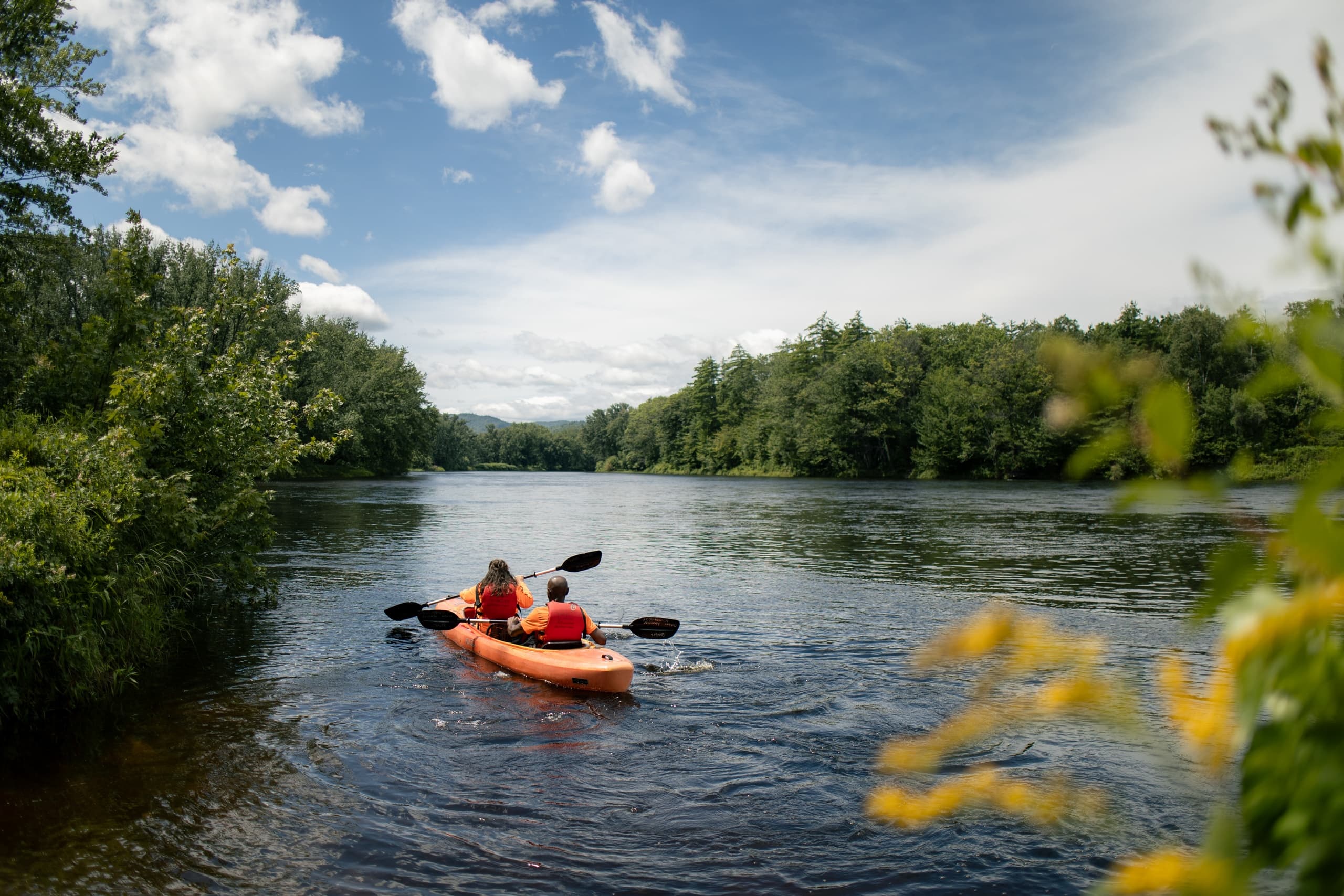 Kayaker paddling an orange kayak on a scenic tree-lined river