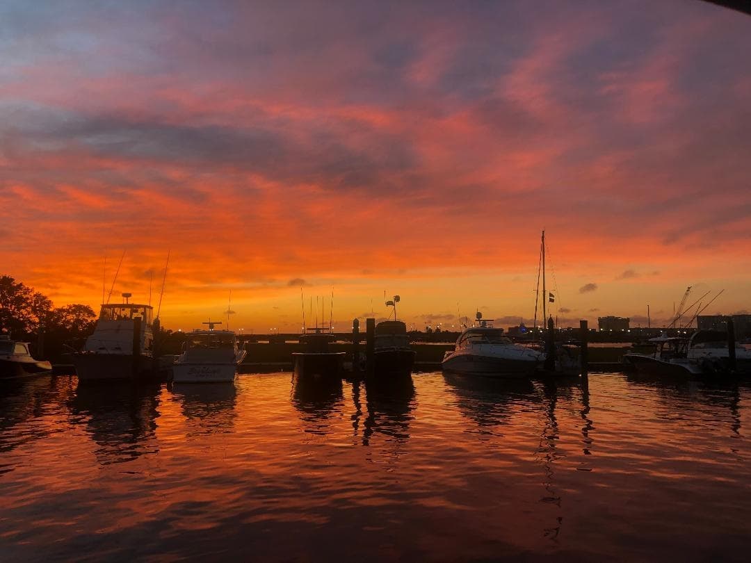 Dramatic sunset over marina with silhouetted boats in harbor