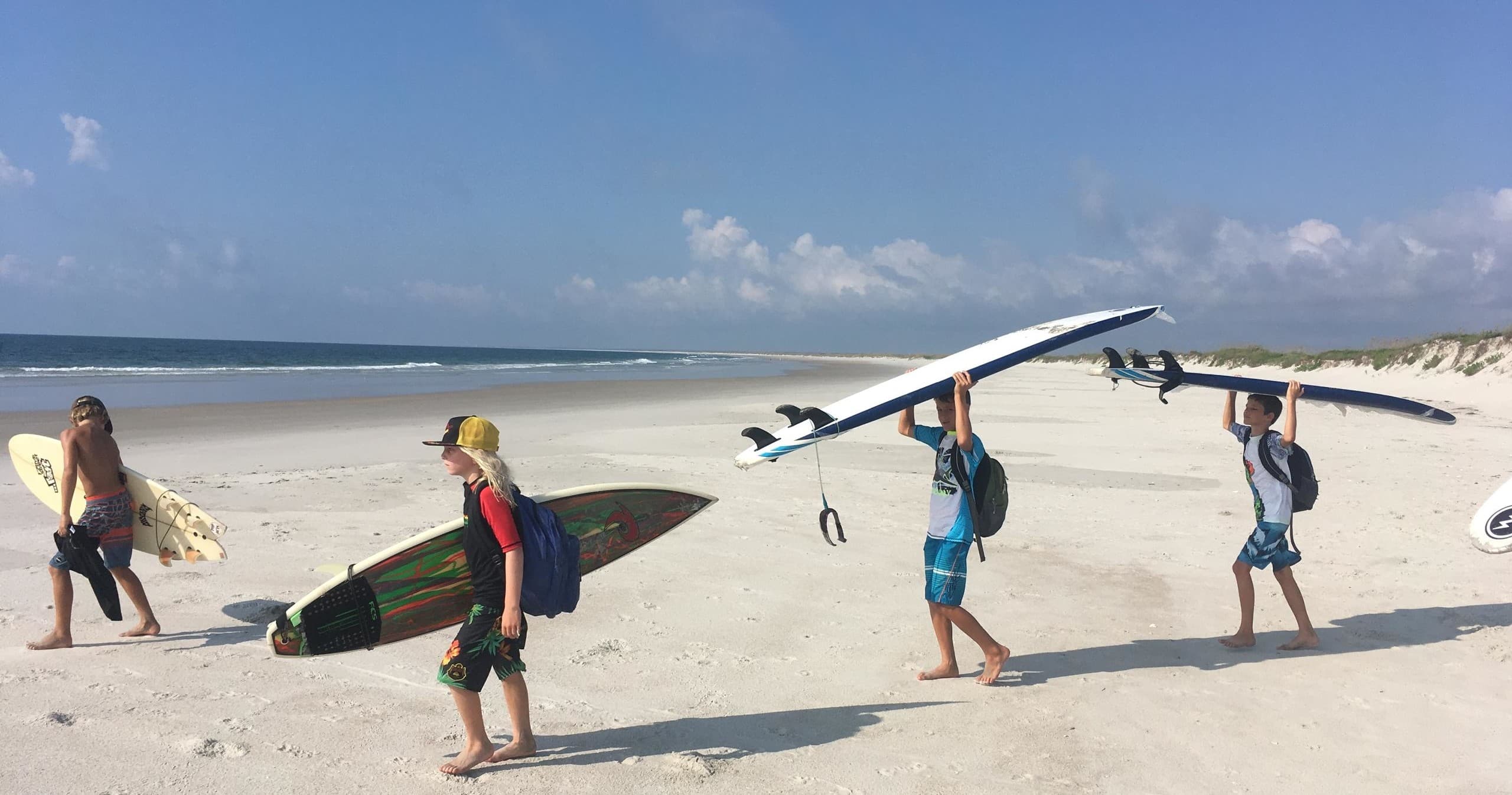 Surfers carrying longboards along sunny white-sand beach