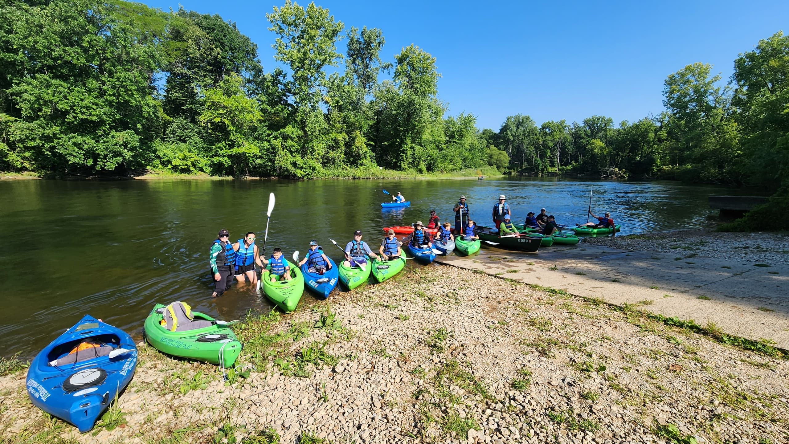 Kayak group on sandy riverbank amid green trees, guided trip