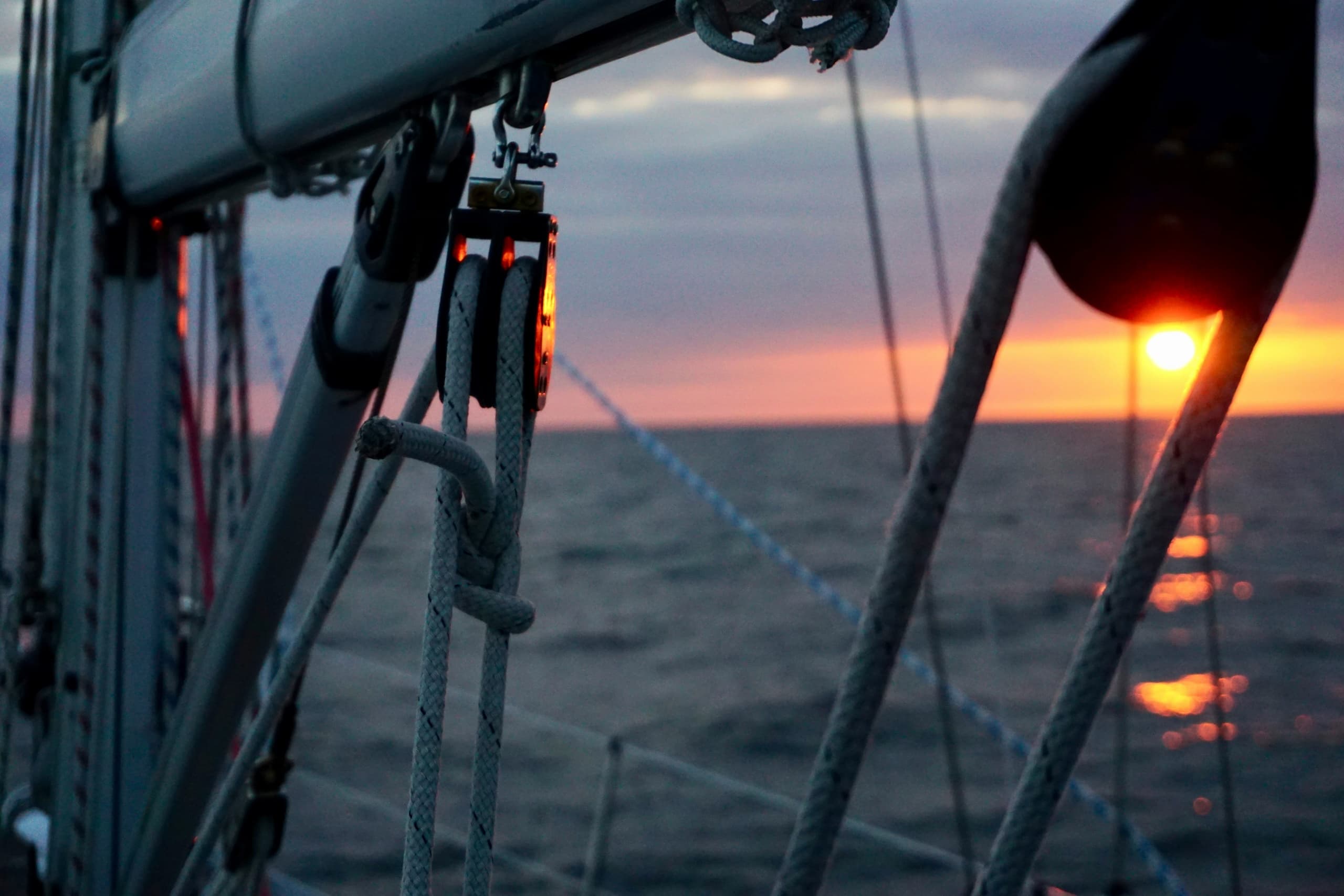 Sailboat rigging silhouetted at sunset over open ocean deck view