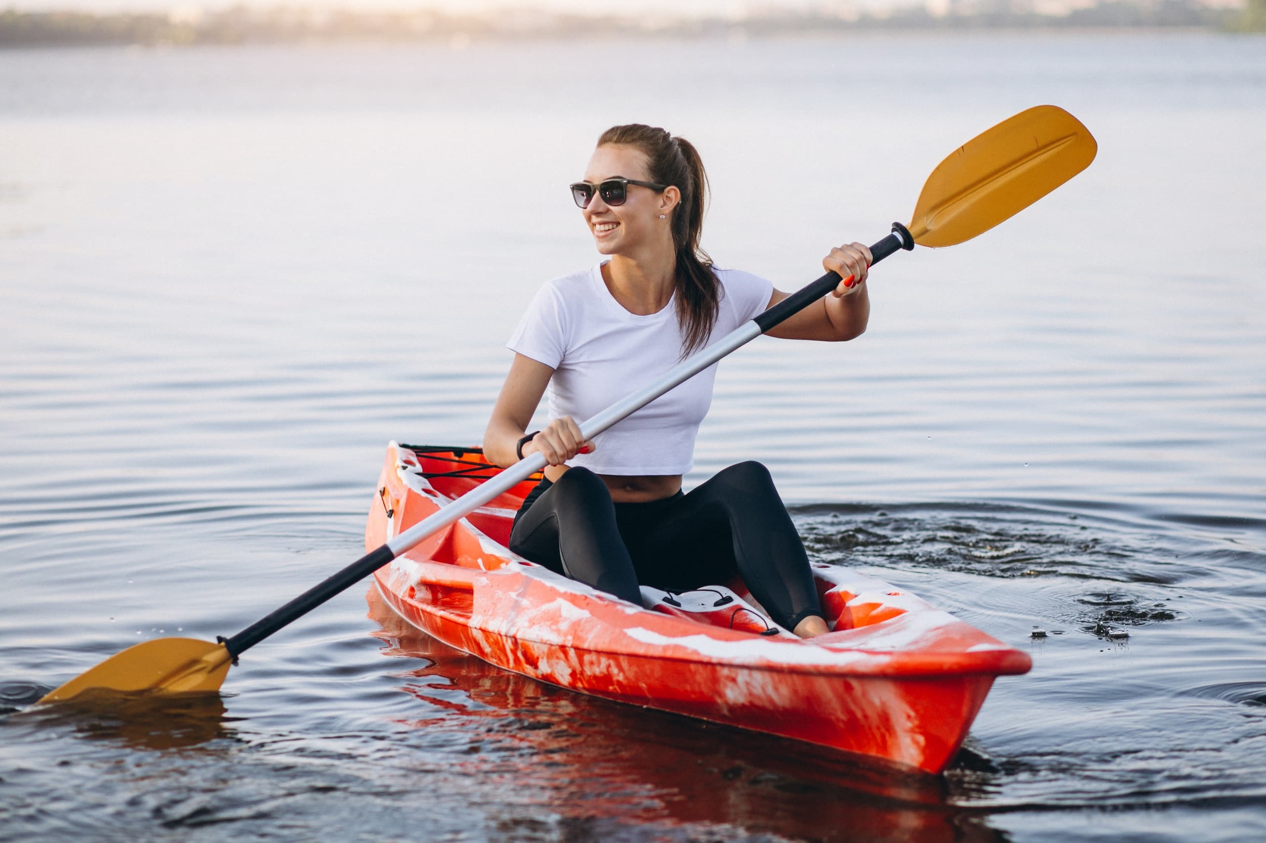 Solo kayaker paddling red kayak across peaceful lake at golden hour