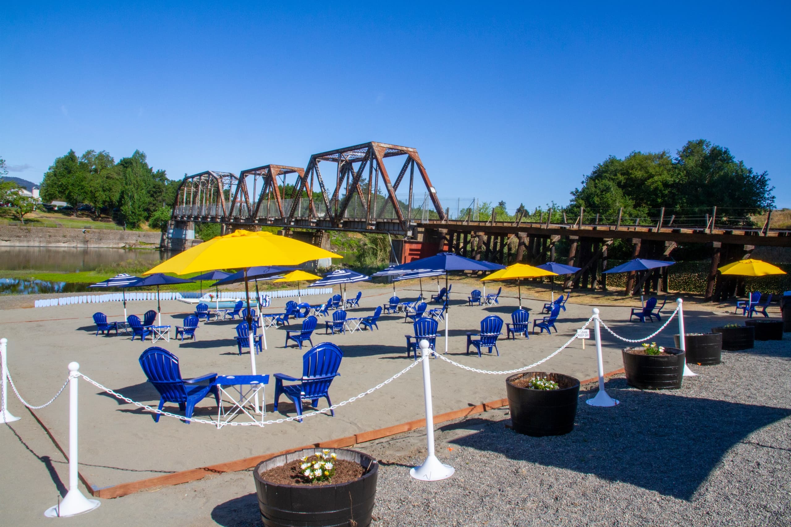 Riverside beach seating with umbrellas and bridge backdrop