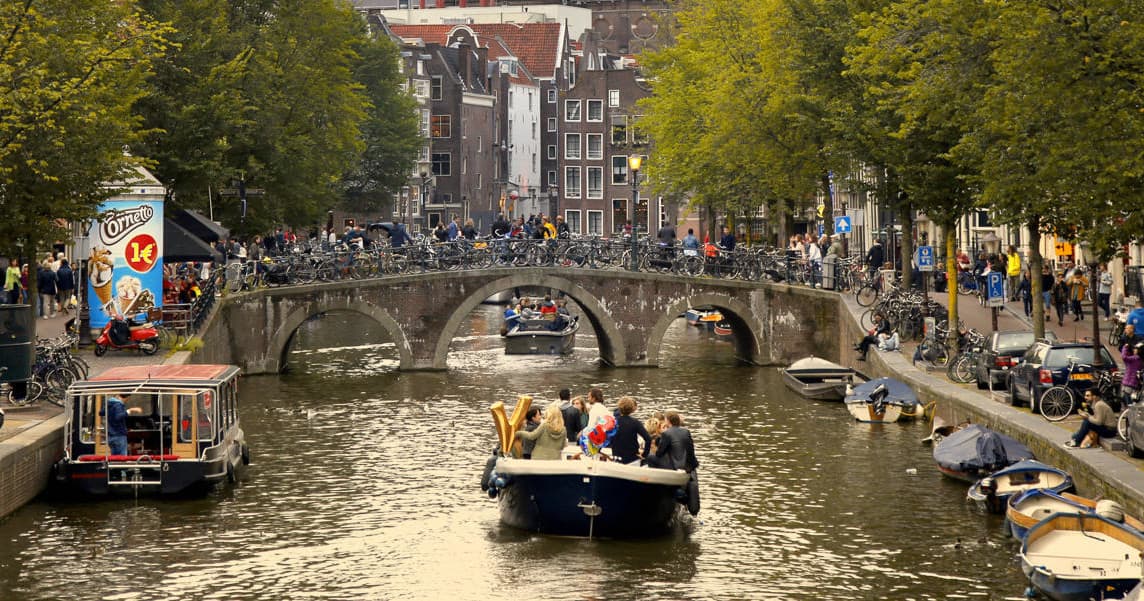 Tour boat cruising Amsterdam canal past historic bridges