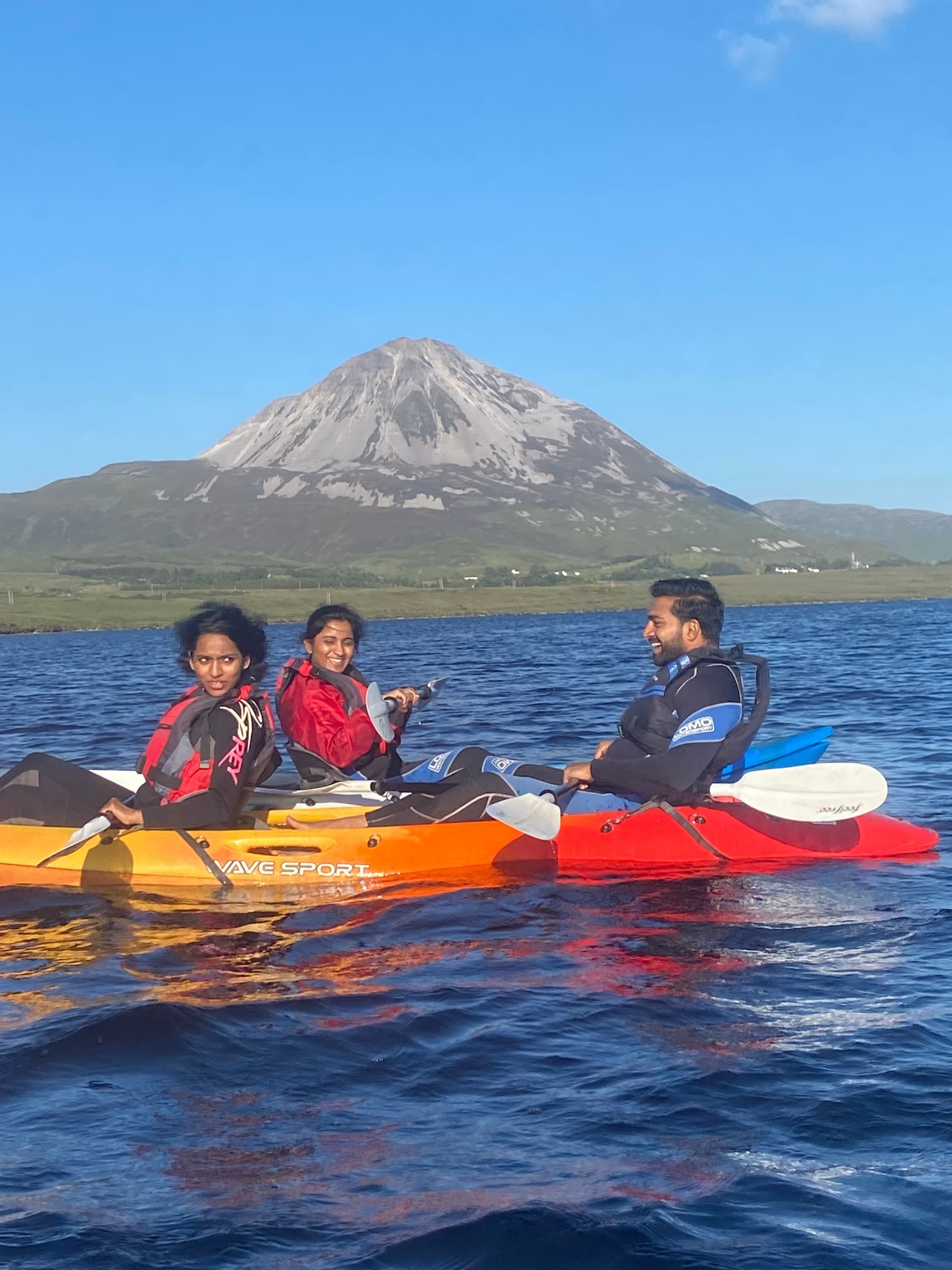Two kayakers smiling with mountain backdrop on blue lake