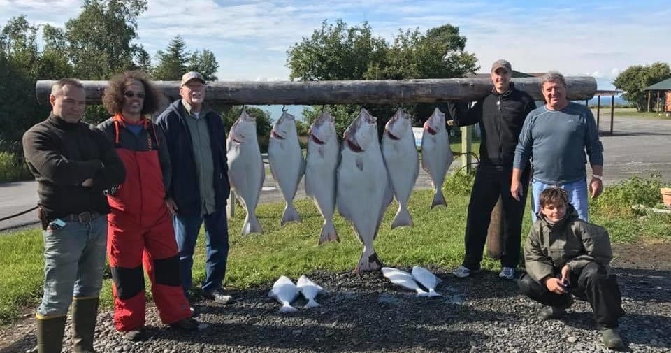 Group of anglers posing with large halibut catch at lodge yard