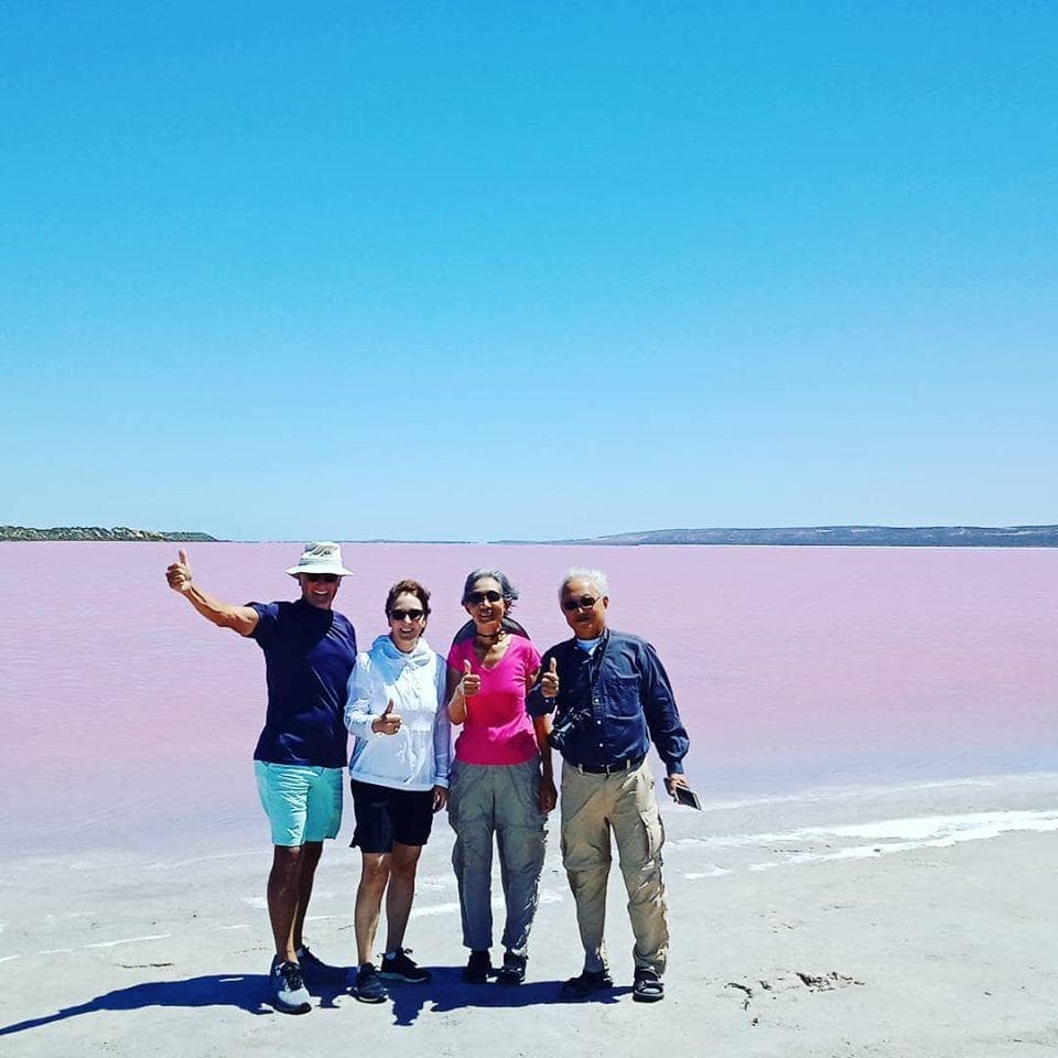 Group posing by pink salt lake shore, social outdoor tour
