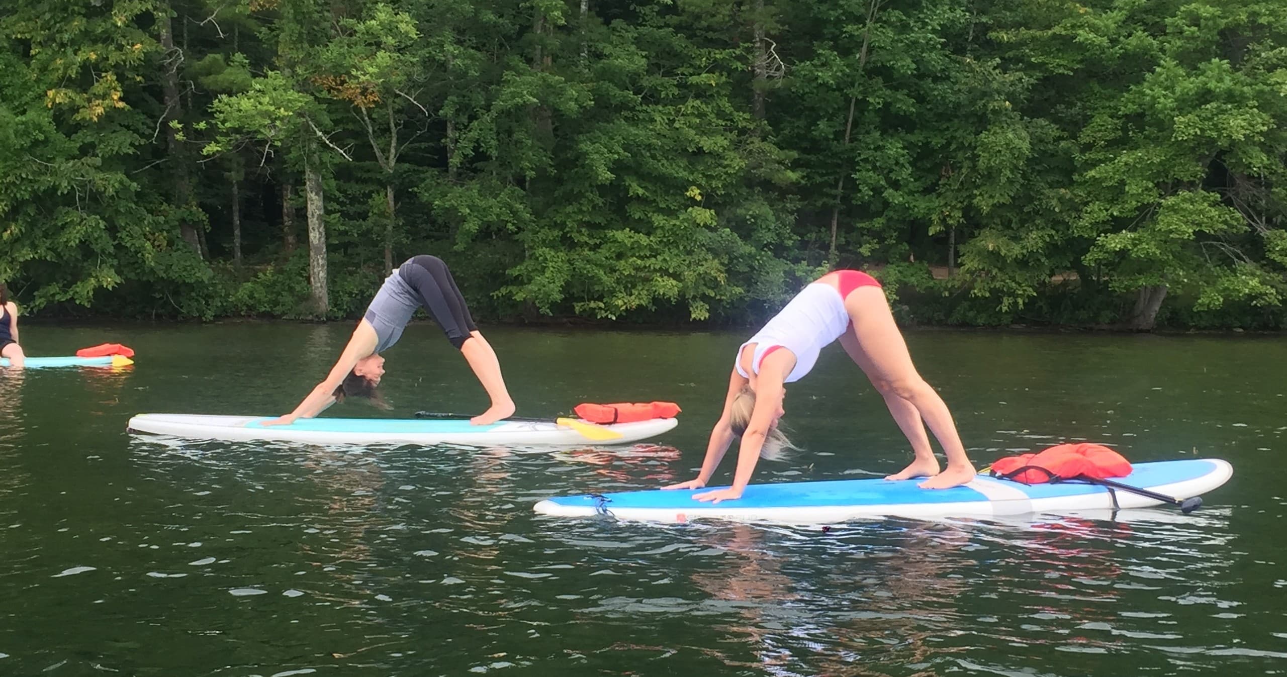Stand-up paddleboard yoga on calm lake with forest shoreline
