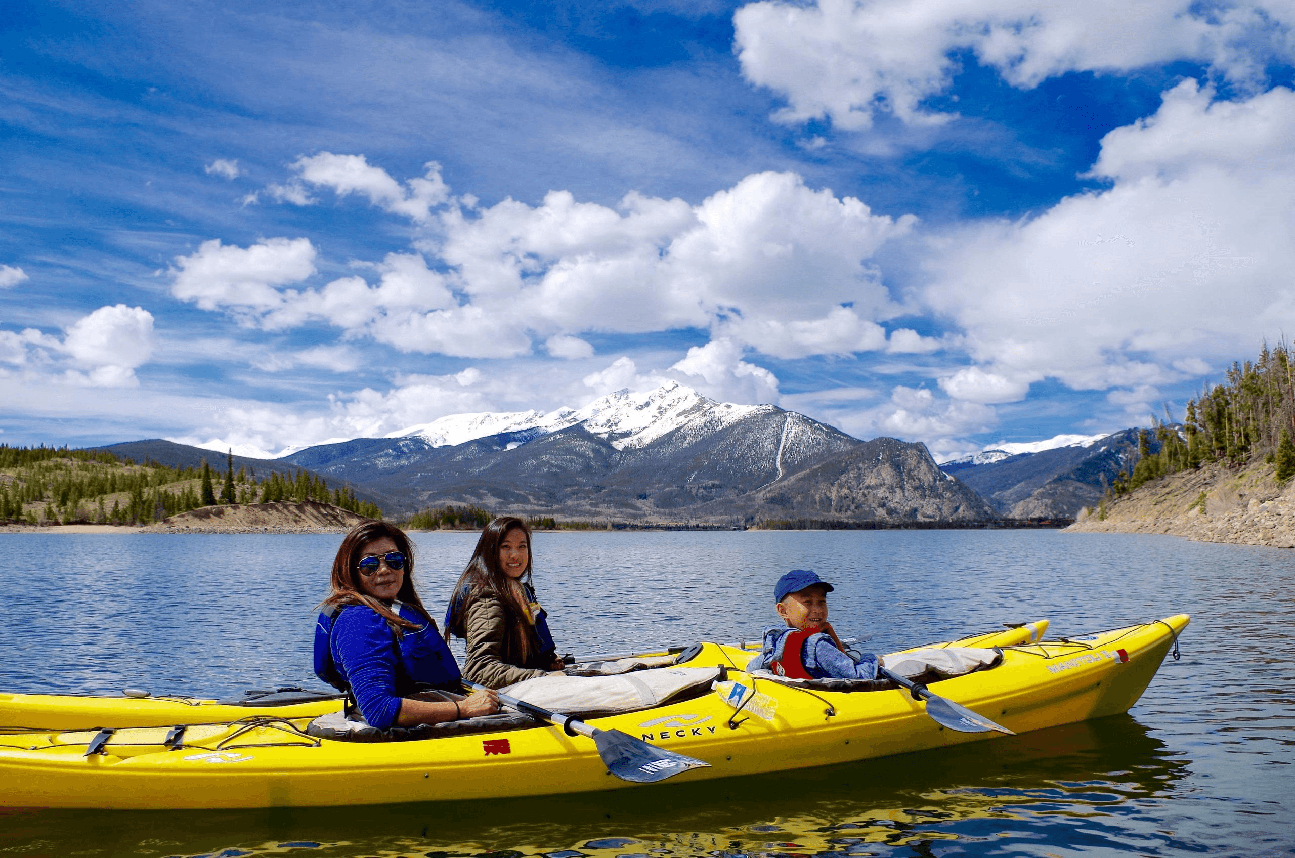 Family kayaking on lake with snowy peaks and blue sky
