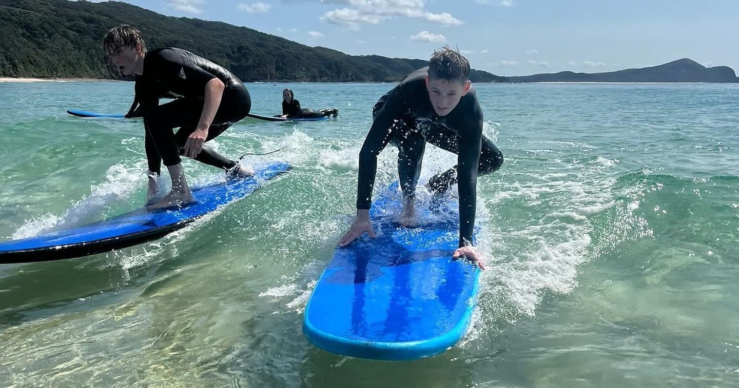 Beginners surfing on blue foam boards in clear coastal waves