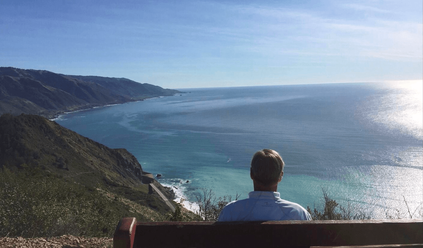 Solo hiker seated at overlook above an expansive coastal bay viewpoint