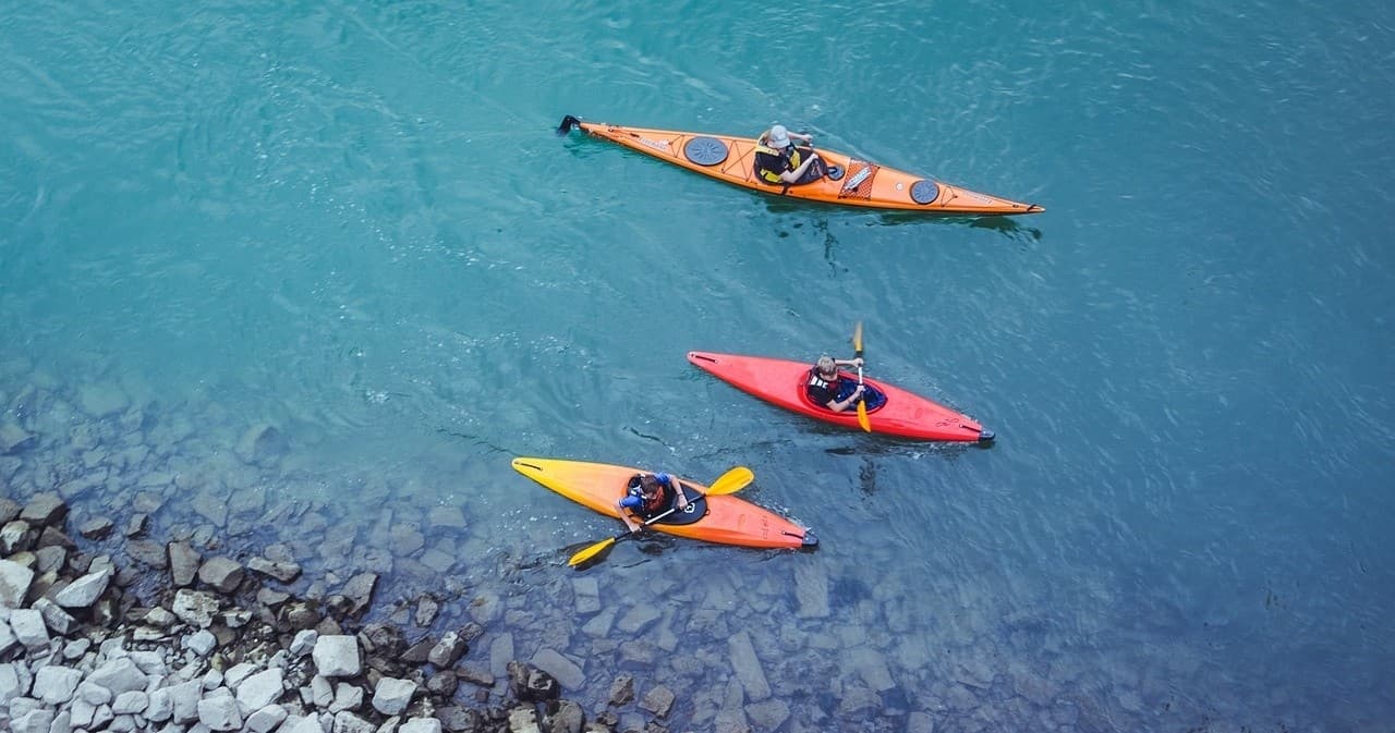 Aerial view of colorful kayaks paddling along rocky turquoise shore