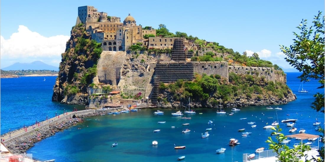 Historic coastal castle island with moored boats, Italian sea