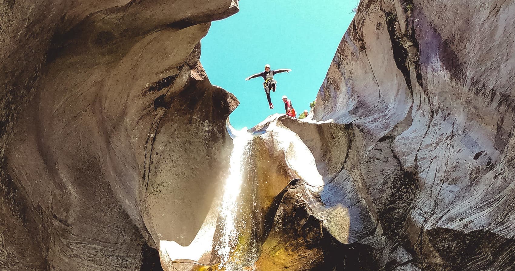 Adventurer jumping between narrow canyon walls into bright sky