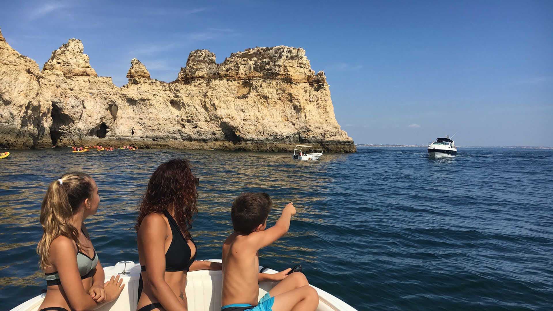 Friends sightseeing from boat toward dramatic coastal cliffs