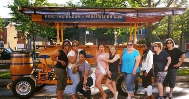 Group of friends posing by pedal wagon on sunny Dayton sidewalk