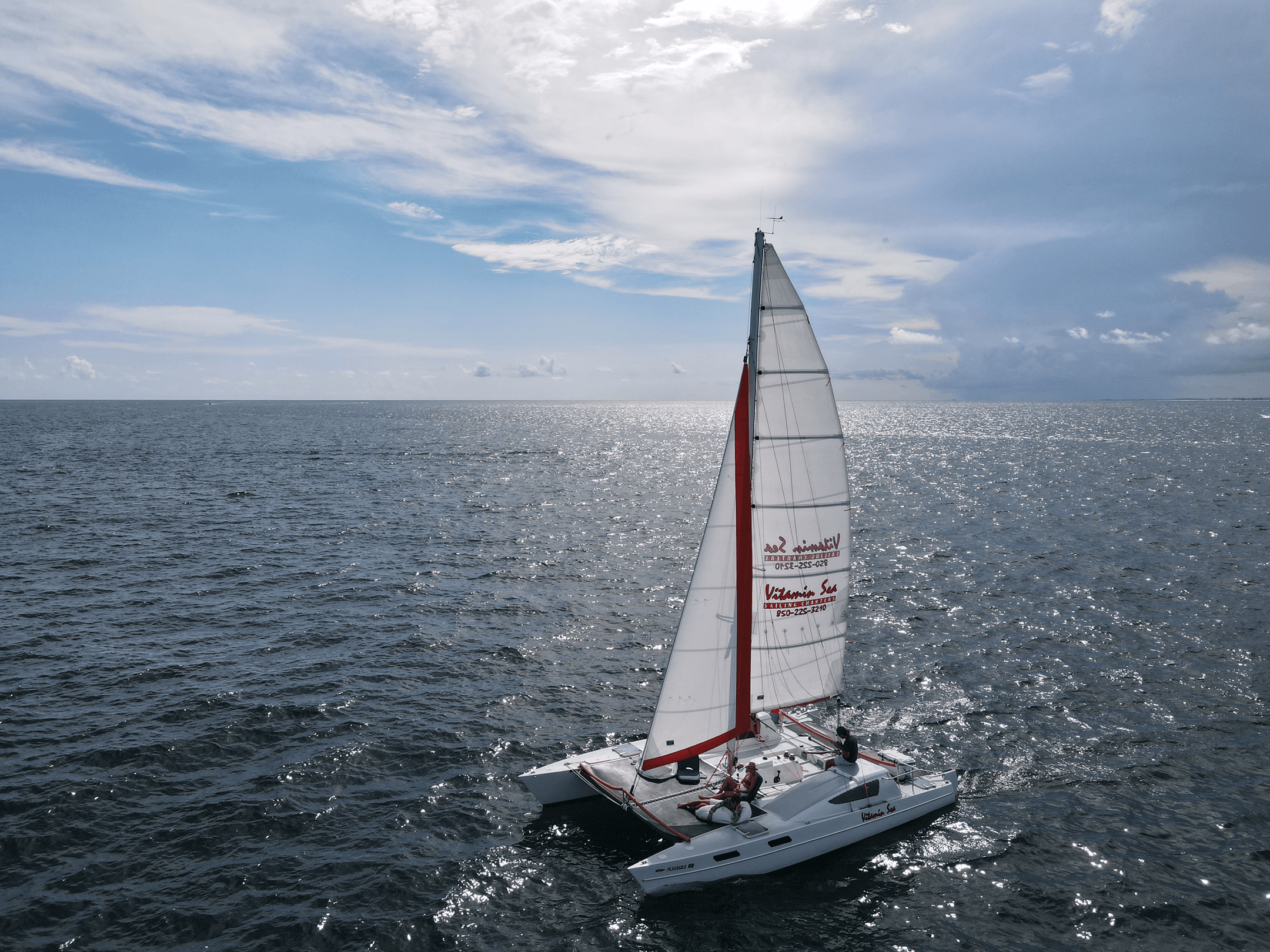 Aerial catamaran sailing on open ocean under dramatic blue sky