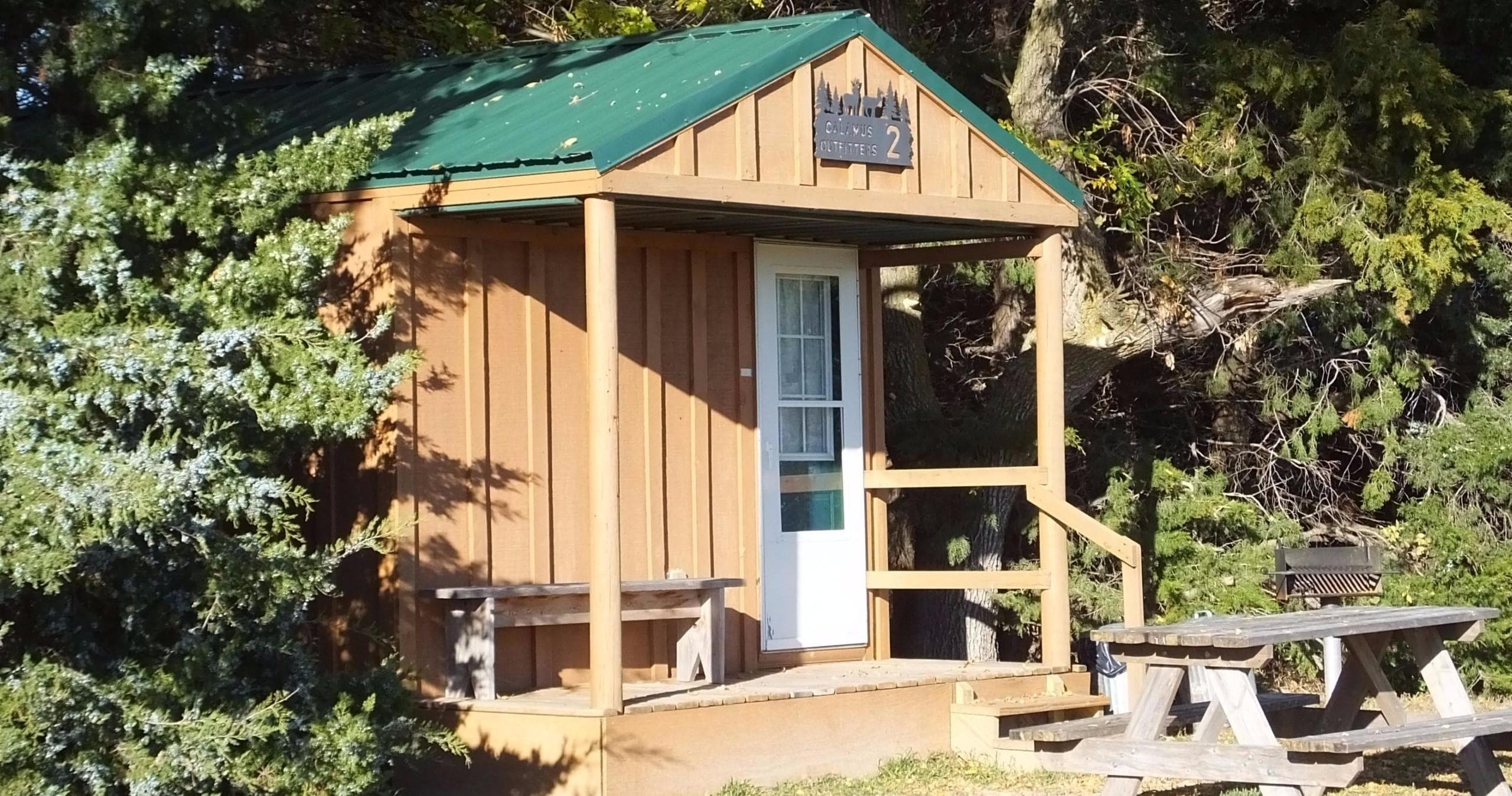 Cozy small wooden camping cabin with picnic table by trees