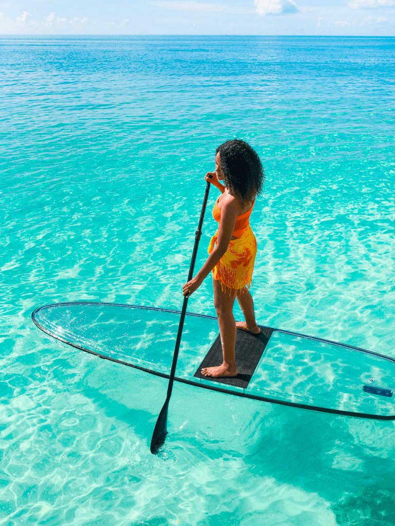 Child standing on clear paddleboard in turquoise tropical water