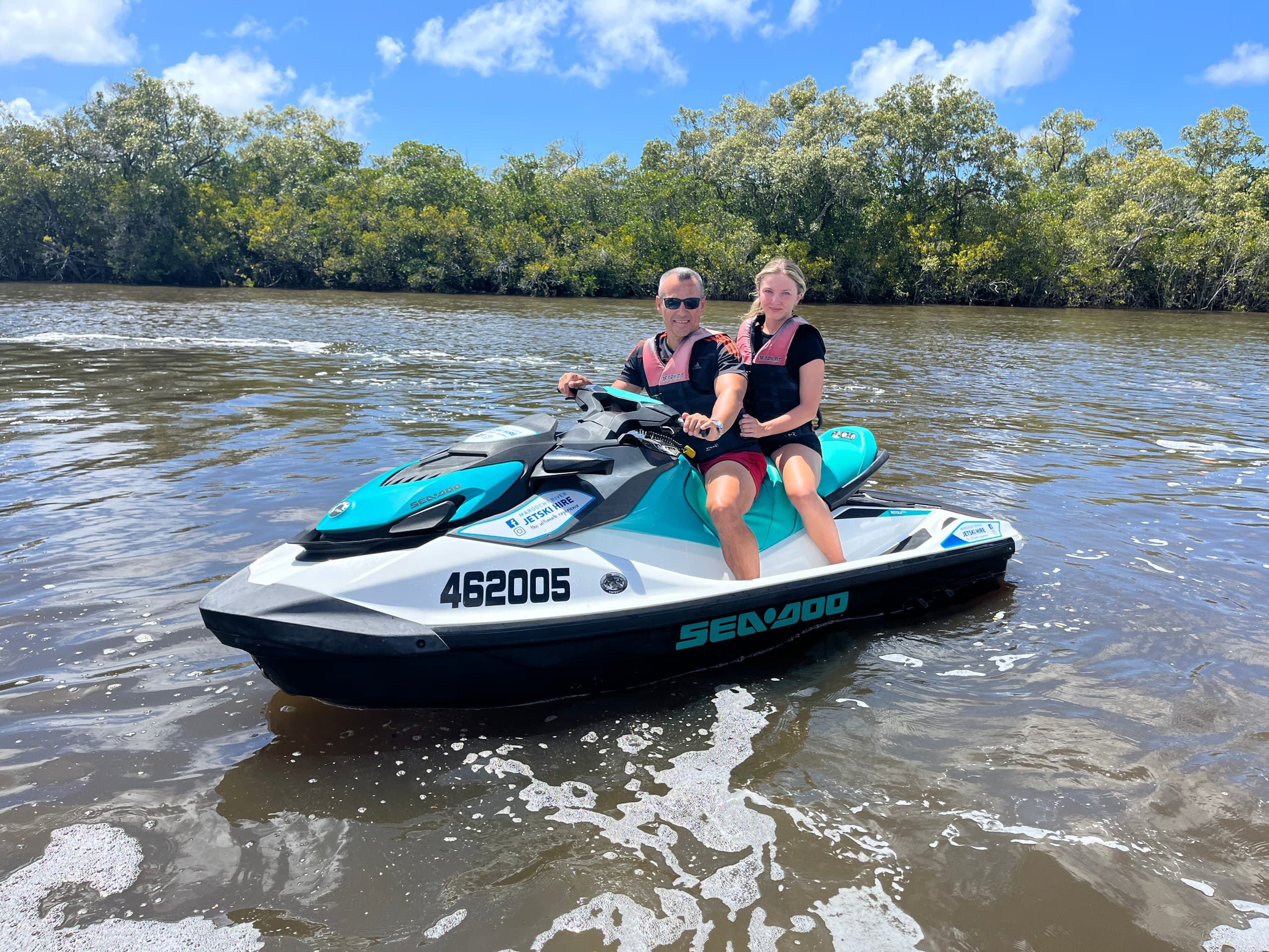 Two riders on jet ski speeding across mangrove lined estuary