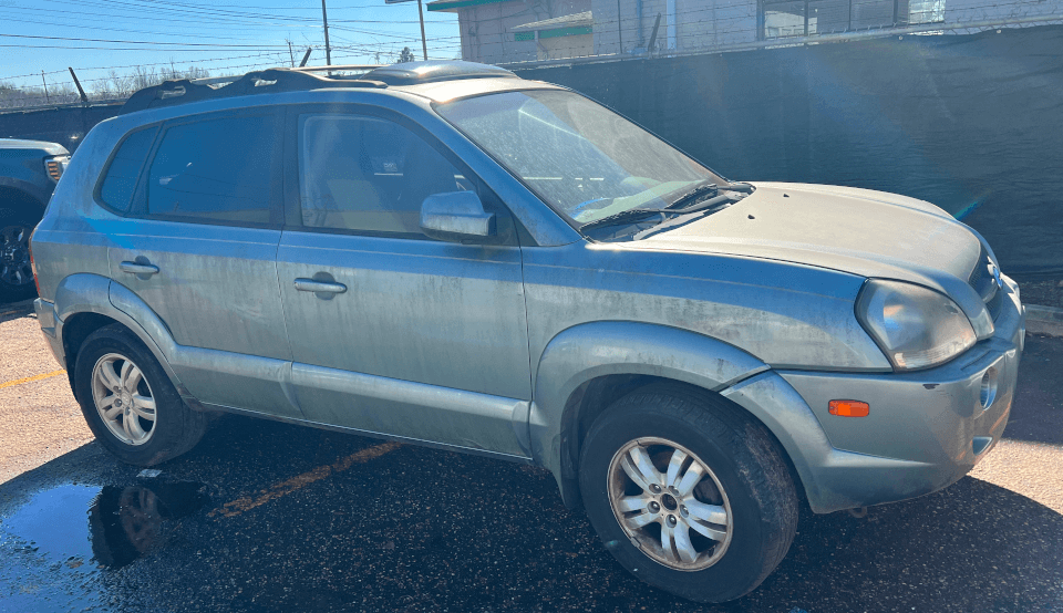 Silver SUV parked outdoors on wet asphalt lot near fence