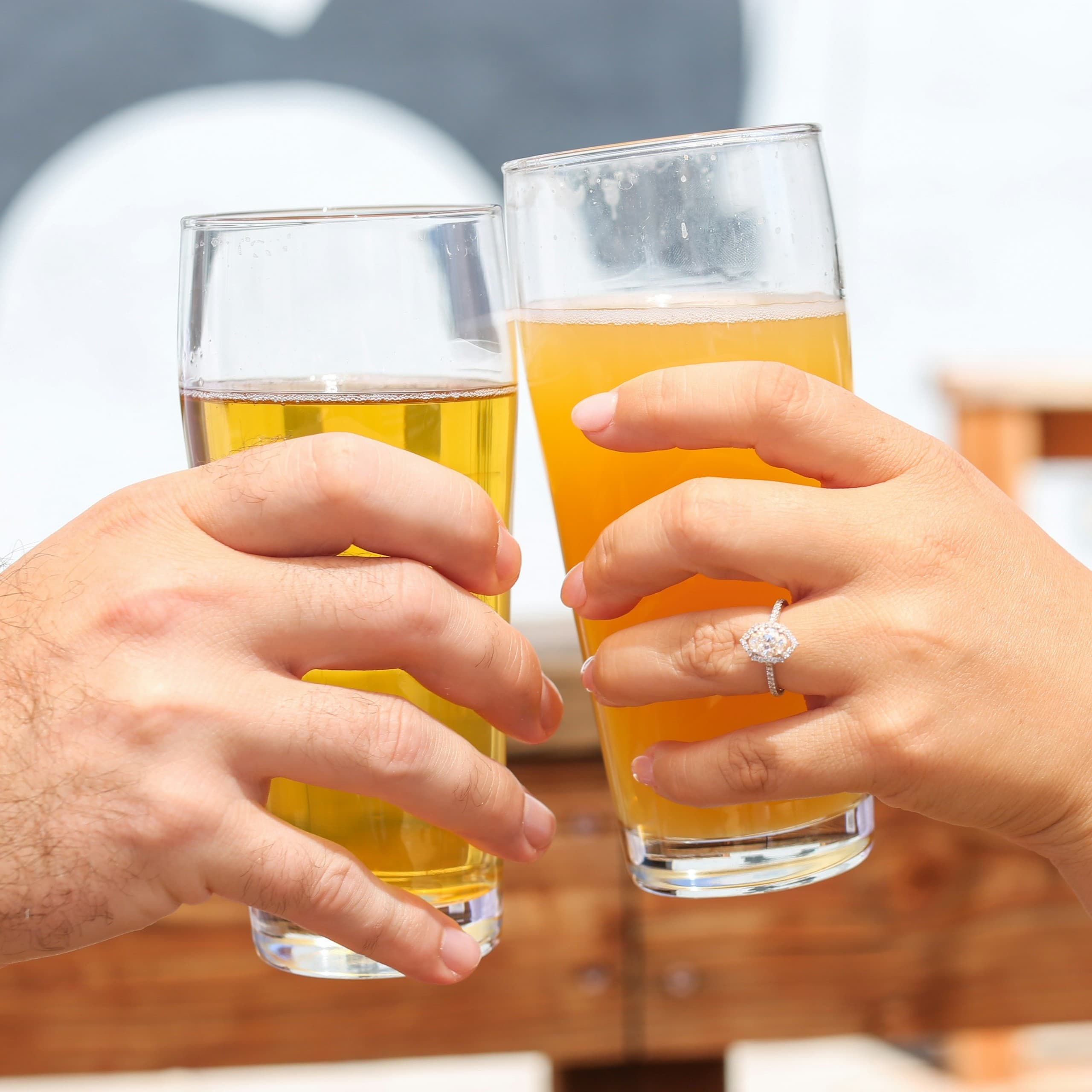 Friends clinking beer glasses outdoors on sunny patio celebration