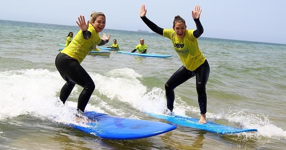 Two instructors guiding learners surfing small waves at Carcavelos