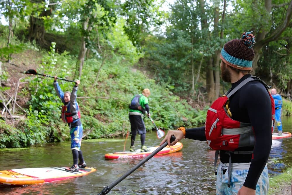 Instructor and group stand-up paddleboarders on a tree-lined riverbank