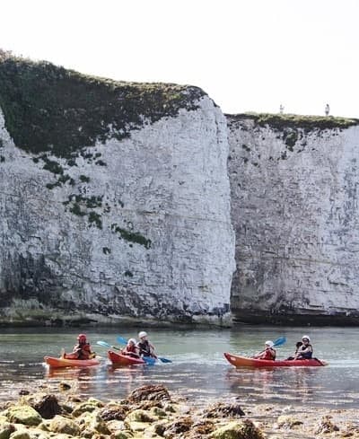 Sea kayakers paddling calm water by chalk sea cliffs