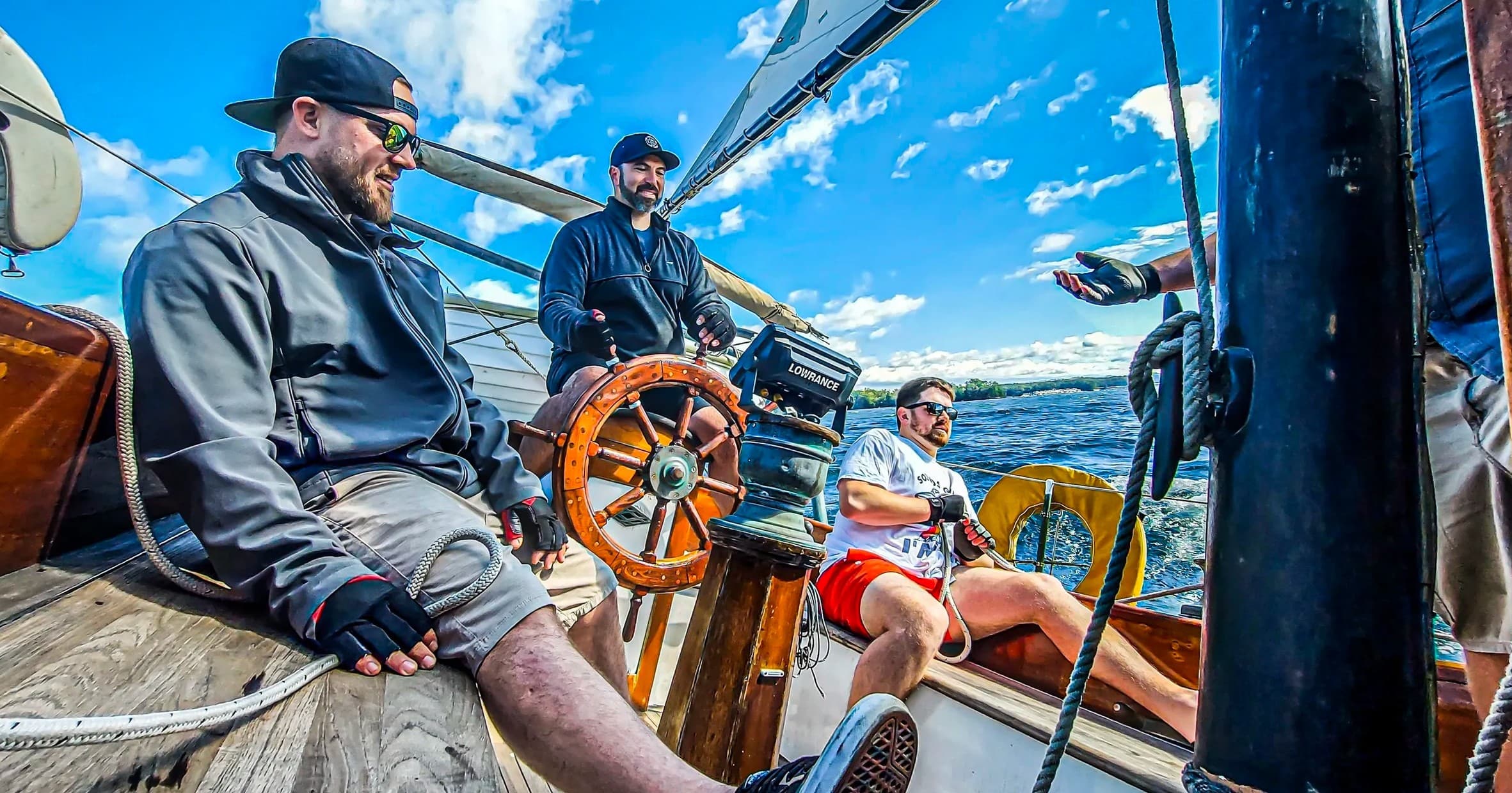 Friends sailing on wooden yacht steering at the helm