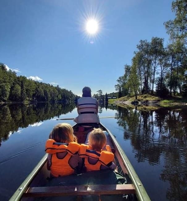 Adult guiding two children in canoe on peaceful reflective river