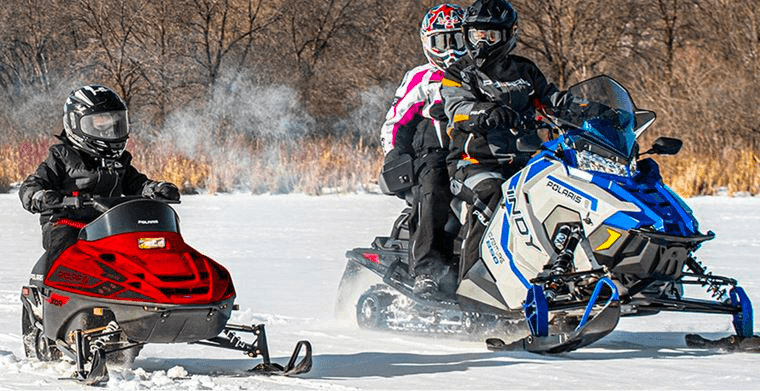Group of snowmobilers riding across frozen field, guided tour