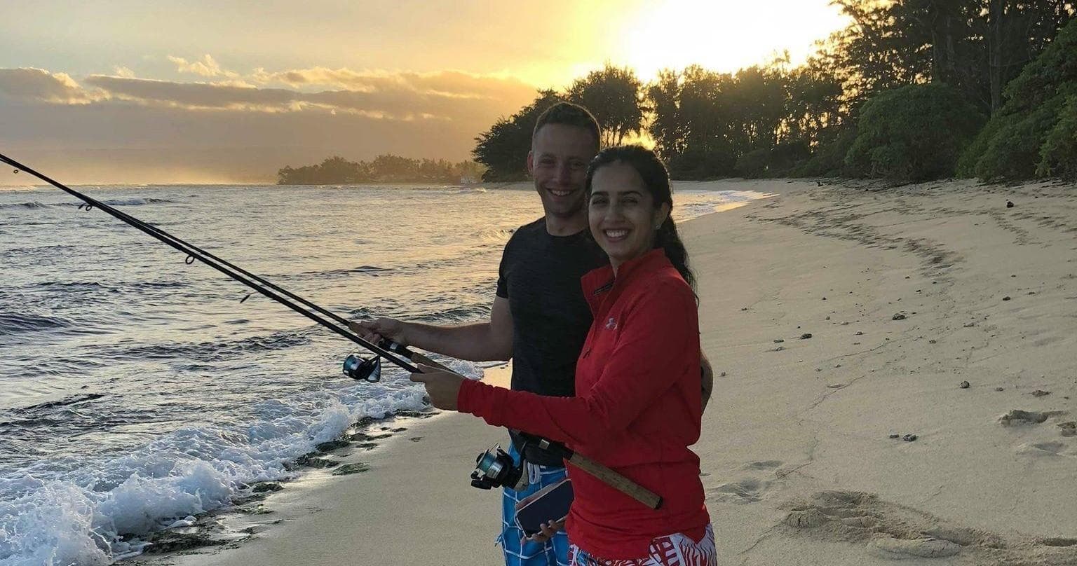Couple surf-fishing on sandy beach at sunset in tropical shore