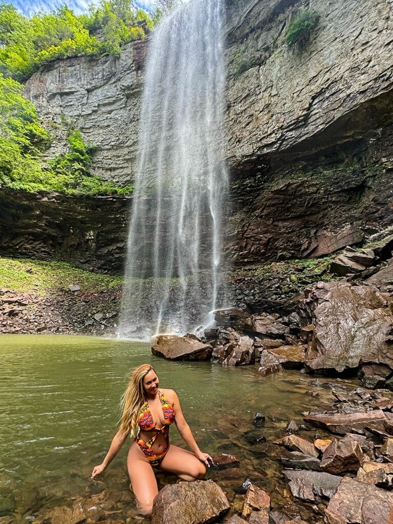 Hiker sitting at base of secluded waterfall pool in rocky canyon