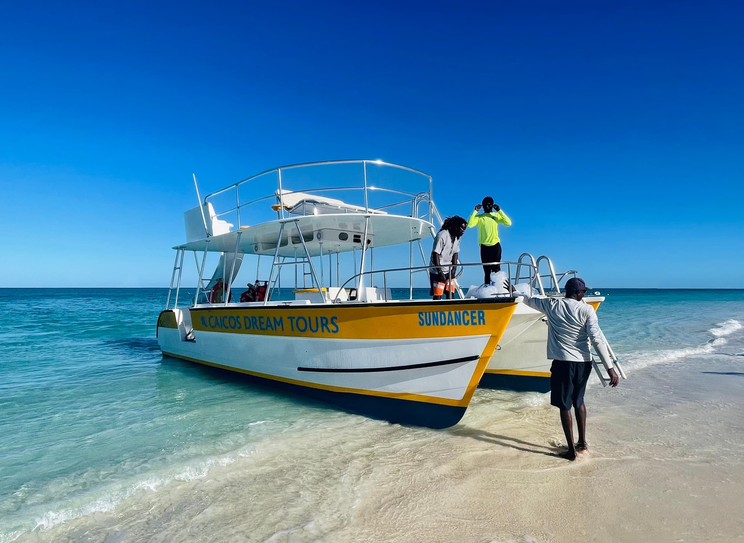 Beached excursion boat with crew on white sand under deep blue sky