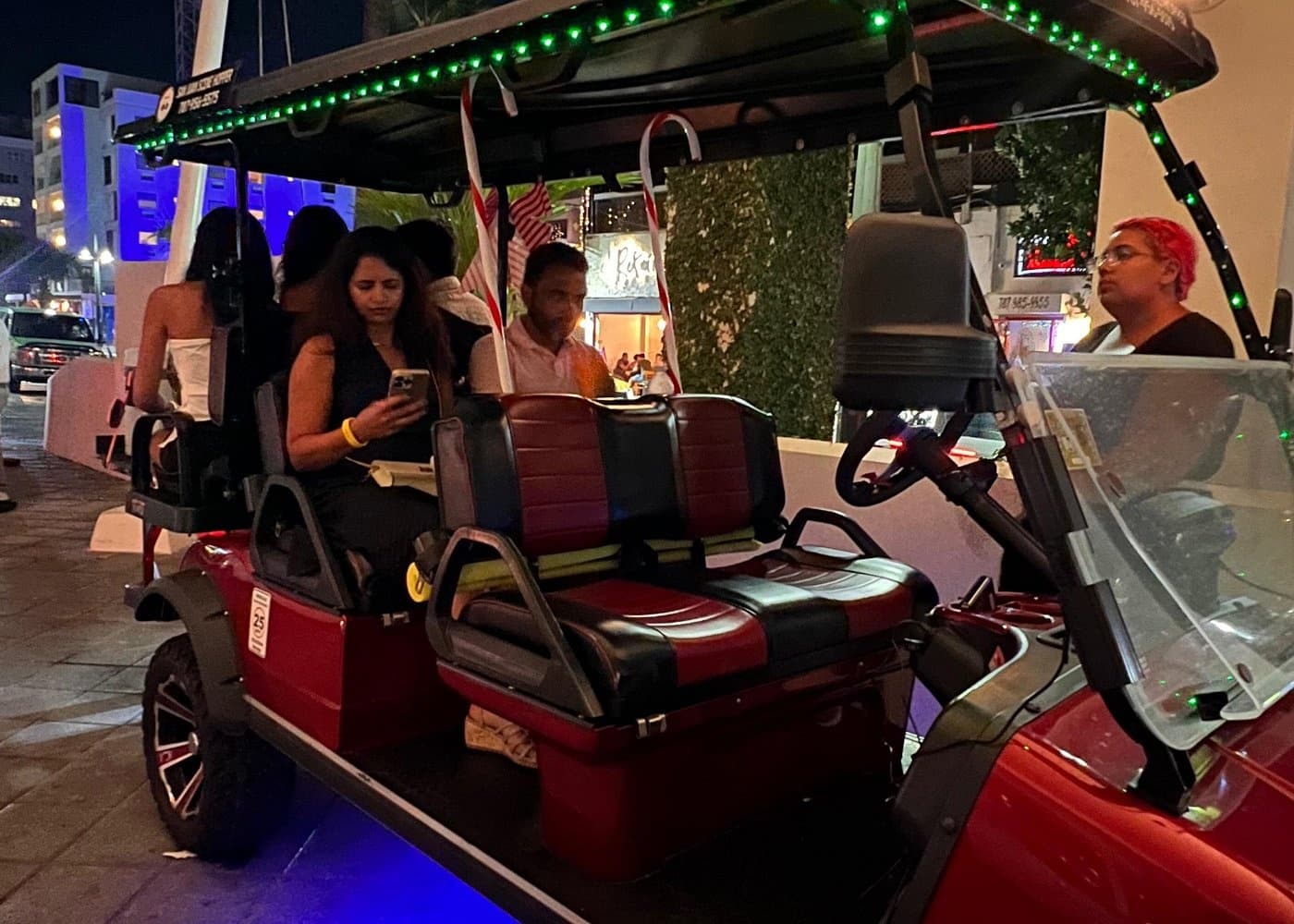 Group riding red open-air golf cart on city street at night