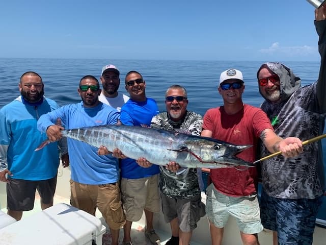Group deep-sea anglers on boat displaying large wahoo in ocean
