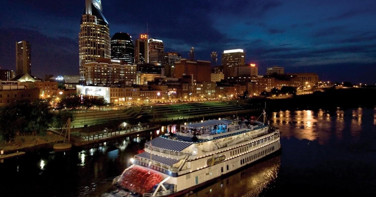 Riverboat cruising past illuminated downtown skyline at night