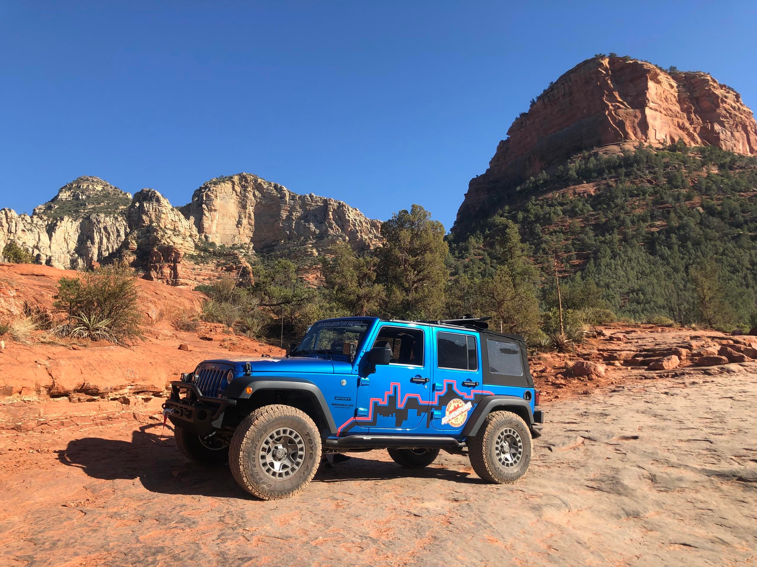 Blue Jeep on red rock plateau with canyon backdrop, trail exploration
