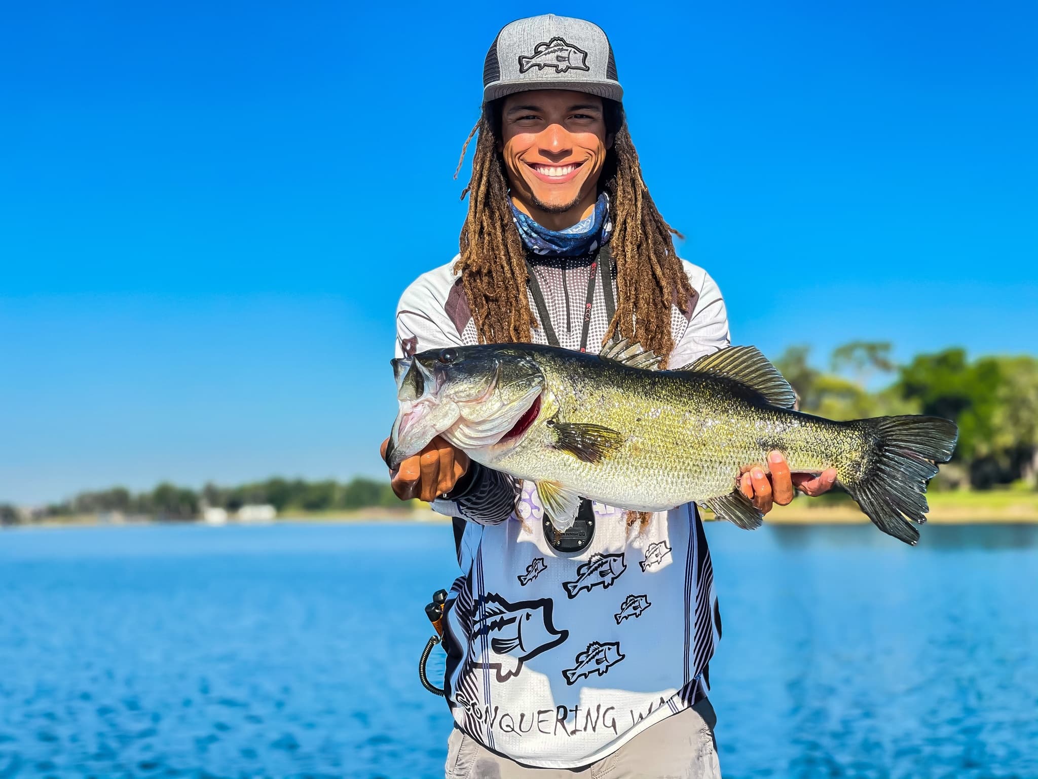 Angler holding largemouth bass on sunny lake shore