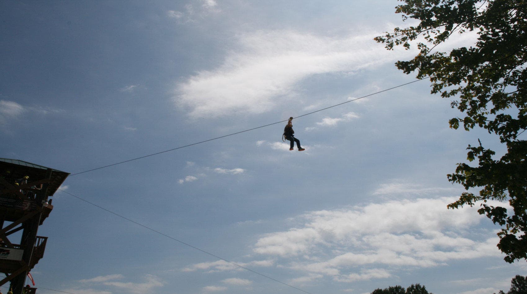 Silhouetted zipliner gliding across sky at ropes adventure park